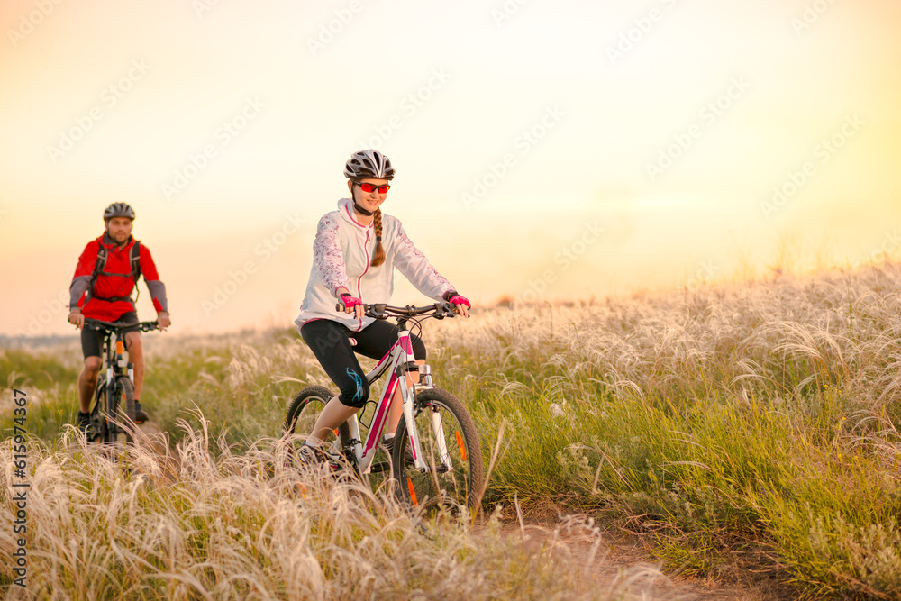 Young Couple Riding the Mountain Bikes in the Beautiful Field Full of Feather Grass at Sunset. Adventure and Family Travel Concept.