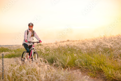 Young Woman Riding the Mountain Bikes in the Beautiful Field Full of Feather Grass at Sunset. Adventure and Travel Concept.