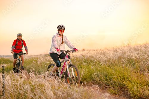 Young Couple Riding the Mountain Bikes in the Beautiful Field Full of Feather Grass at Sunset. Adventure and Family Travel Concept.