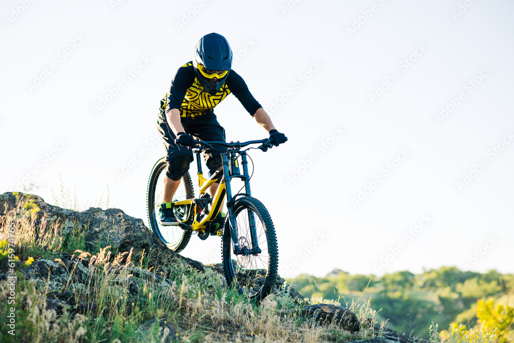 Naklejka premium Professional Cyclist Riding the Downhill Mountain Bike on the Summer Rocky Trail at the Evening. Extreme Sport and Enduro Cycling Concept.