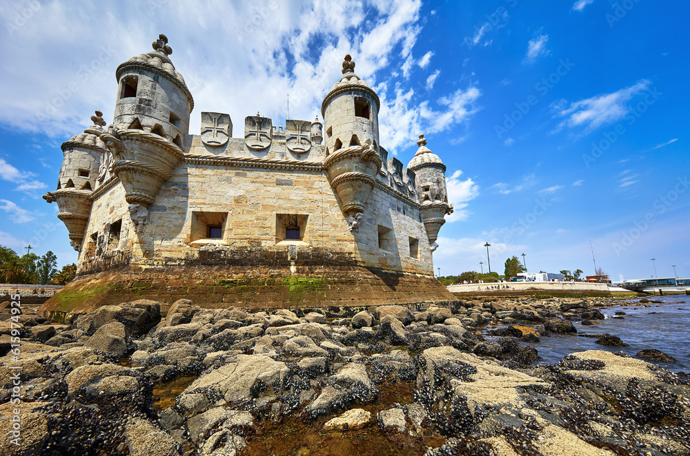 Lisbon, Portugal. Tower Belem at coast of river Tagus. Stones and mussels day during low tide blue sky with clouds. Lisbon, Portugal. Tower Belem at coast of river Tagus. Stones and mussels day during low tide blue sky with clouds.