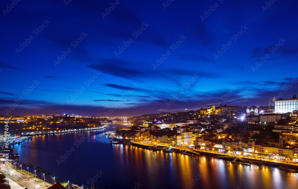 Porto, Portugal. Evening sunset panoramic view at nighttime town. Coastline of river Douro with reflections of illumination in water and picturesque clouds on blue sky.