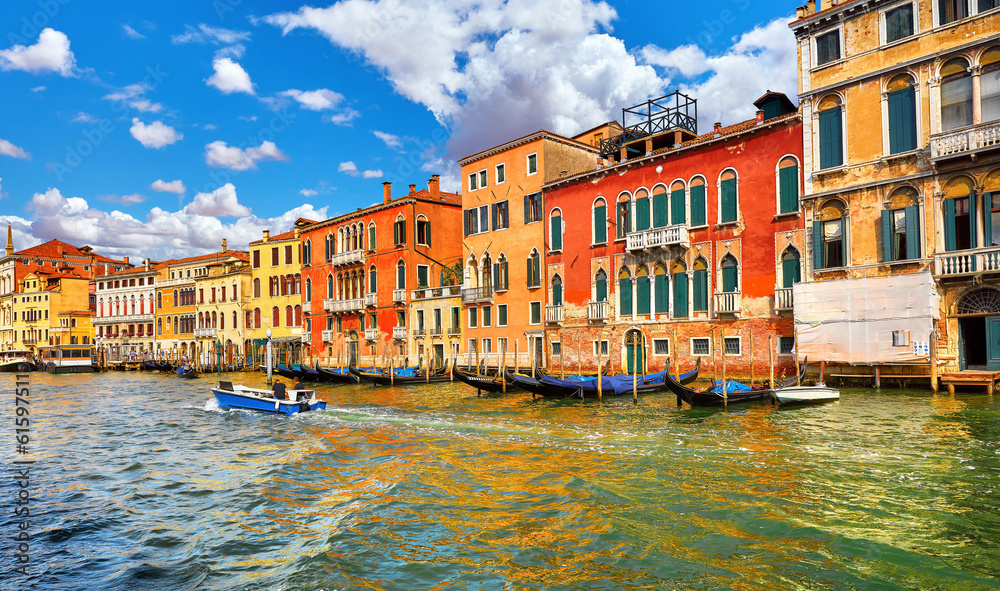 Venice, Italy. Motorboat floating by Grand Canal among antique buildings and traditional italian Venetian architecture. Sunny day with blue sky and clouds.