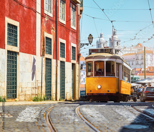 Lisbon, Portugal. Vintage yellow retro tram on narrow bystreet tramline. Red houses in Alfama district of old town. Popular touristic attraction of Lisboa city.