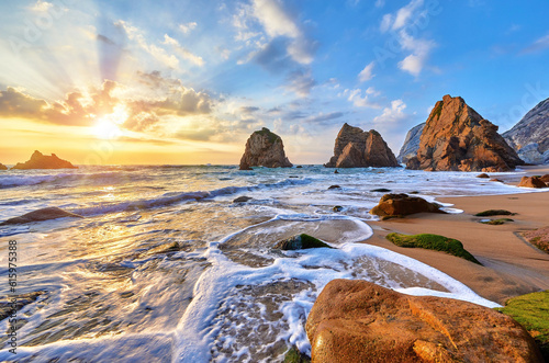Portugal Ursa Beach at atlantic coast of Atlantic Ocean with rocks and sunset sun waves and foam at sand of coastline picturesque landscape panorama. Stones with green moss in front.