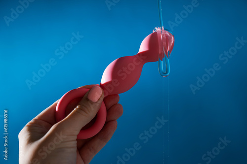 Woman pouring lubricant on pink anal beads on blue background. 