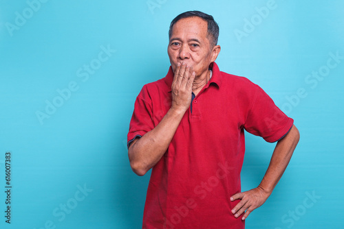Shocked elderly Asian man covering mouth with hand for mistake isolated on blue background