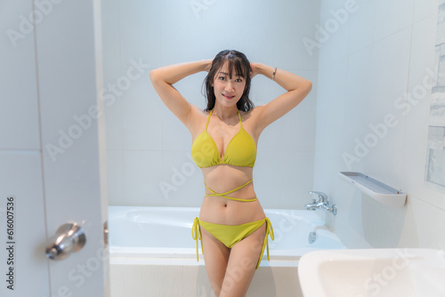 Sexy asian woman Wear a yellow bikini on the tub in the bathroom. © releon8211