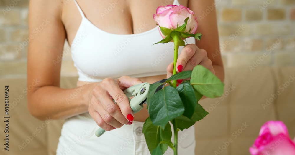 Young woman engaged in floral shop cuts off the roses with a pruner.