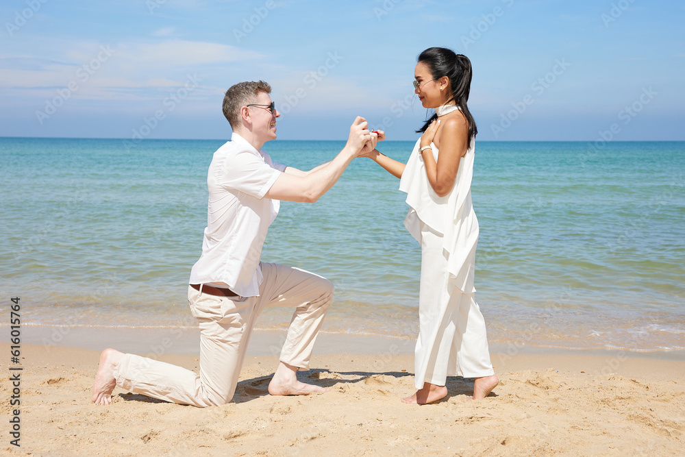 young man showing engagement ring and surprise his girlfriend on the beach