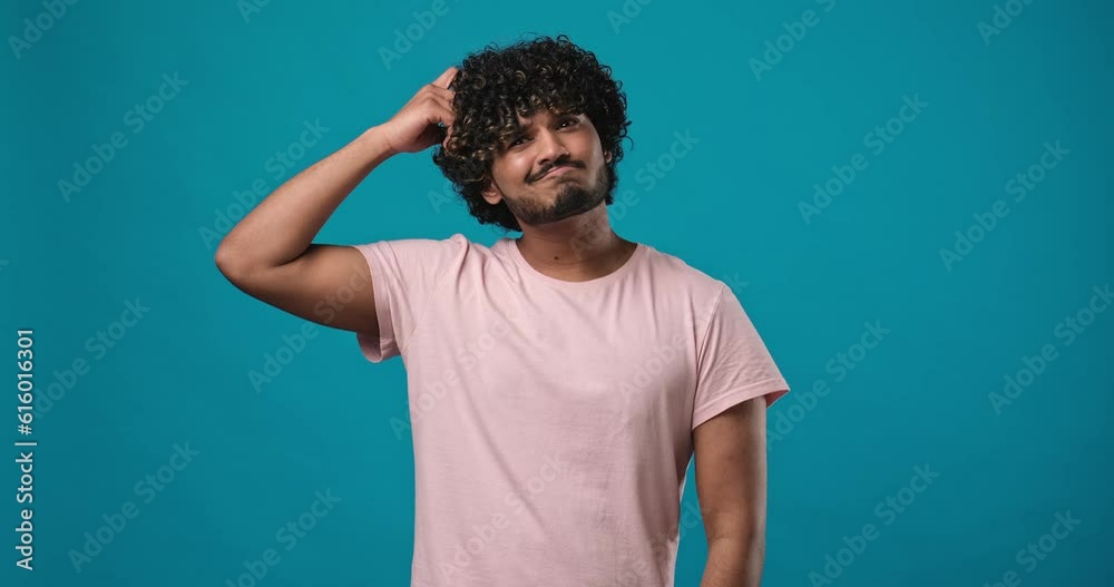 Pensive Young indian man thinking scratching head and shrug showing dont know gesture standing isolated over blue studio background Pensive Young indian man thinking scratching head and shrug showing dont know gesture standing isolated over blue studio background