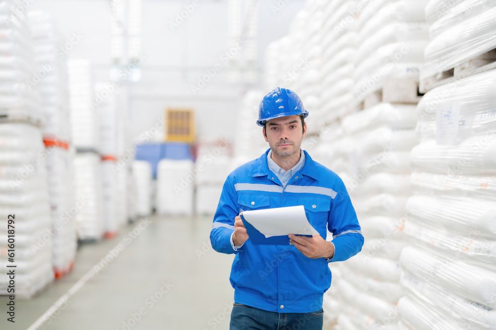half body photo of American male engineers Look smart, send eye contact. In a large warehouse, holding a list note, wearing a helmet, uniform, in a plastic and steel material manufacturing plant