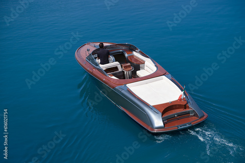 Fashion wooden boat with a man moving on the water aerial view. Luxurious big boat for millionaires slow motion on dark blue water top view. Luxury boat with white leather chairs move on the water.