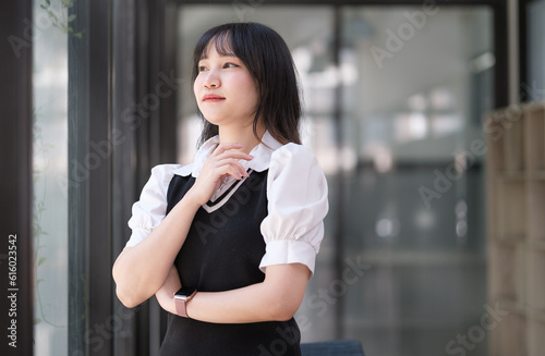 Satisfied young asian woman student headphones standing near glass window and looking thoughtfuly. Free Download Satisfied young asian woman student headphones standing near glass window and looking thoughtfuly. - GFXLoad