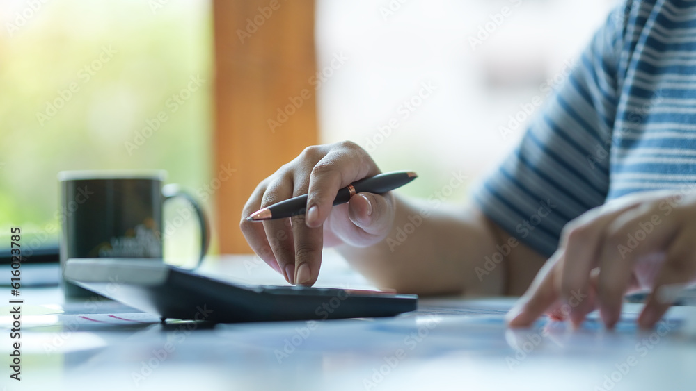 Cropped shot young female accountant using calculator and checking financial reports.
