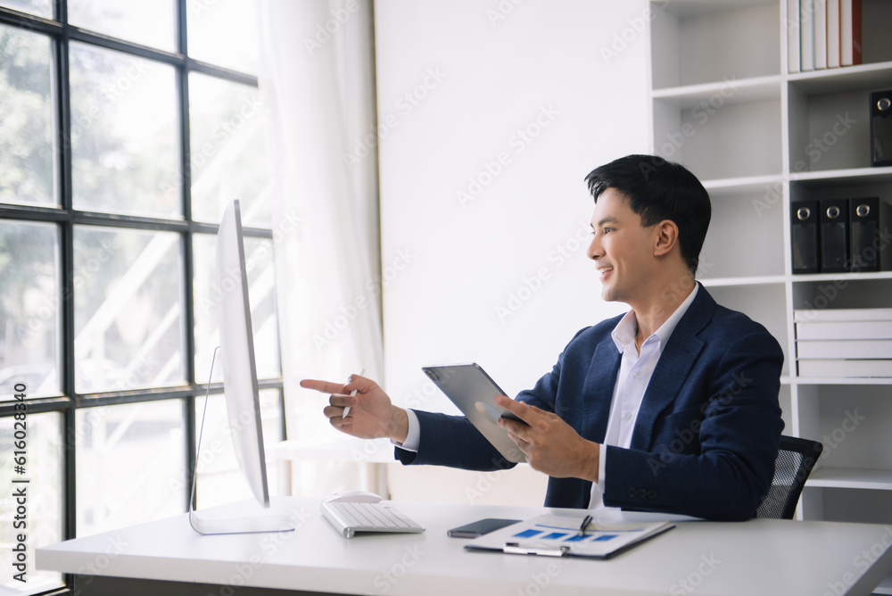 Young Asian business man using laptop and tablet while sitting at her working place. Concentrated at work. Young Asian business man using laptop and tablet while sitting at her working place. Concentrated at work.