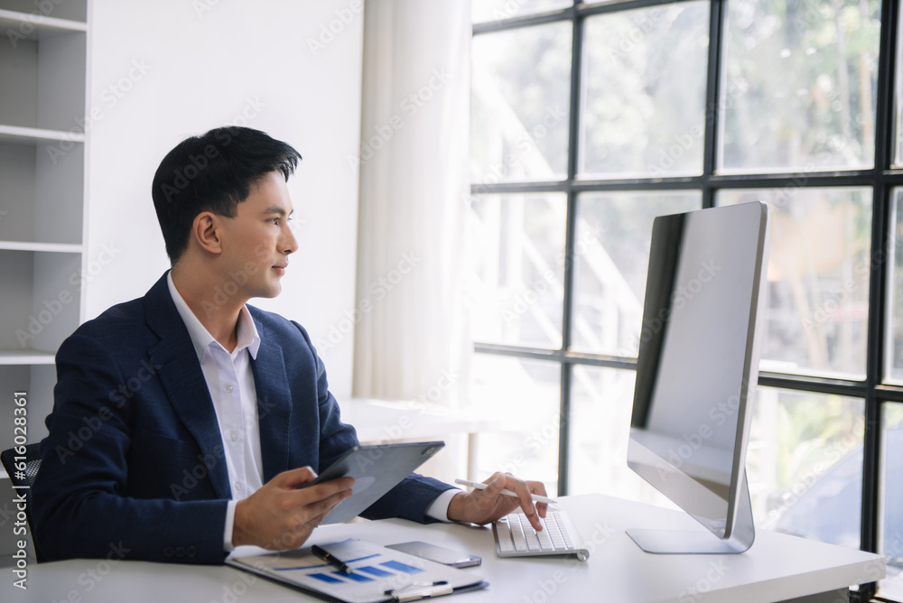 Young Asian business man using laptop and tablet while sitting at her working place. Concentrated at work. Young Asian business man using laptop and tablet while sitting at her working place. Concentrated at work.