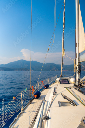 Yacht sailing in an open sea. Close-up view of the deck, mast and sails. Clear sky, waves and water splashes © dtatiana