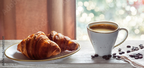 Morning black coffee with crema and fresh hot croissants on a wooden table. French breakfast with a small cup of espresso and view from the window on a sunny day  blurred background with bokeh.