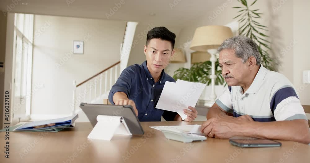 Diverse financial advisor and senior man discussing paperwork and using tablet at home, slow motion Diverse financial advisor and senior man discussing paperwork and using tablet at home, slow motion