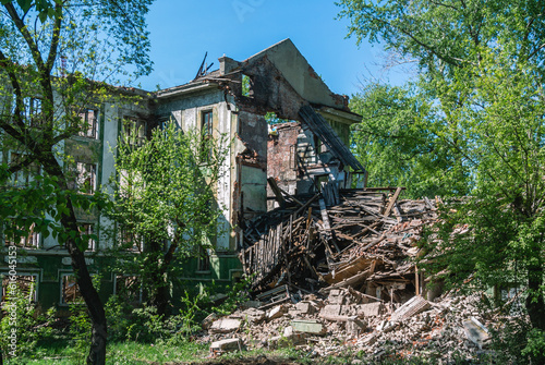 A ruined old house. The collapse of the walls of the house. Dilapidated housing. Demolition of the old building. An old ruined building overgrown with trees.