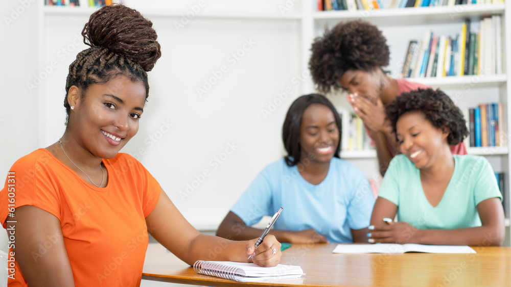 Obraz premium Young black female student at desk with group of learning african american students