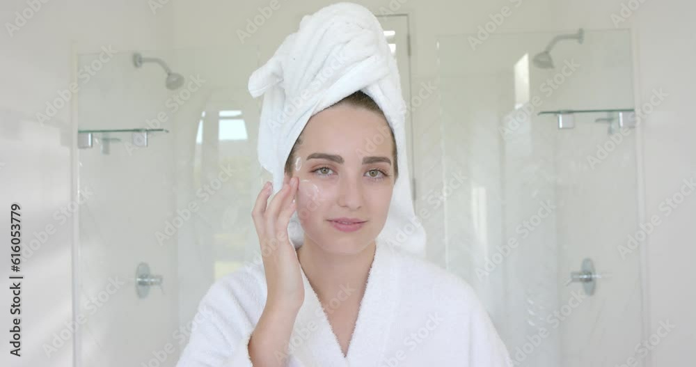 Portrait of caucasian woman with towel on head applying cream on face in bathroom in slow motion Portrait of caucasian woman with towel on head applying cream on face in bathroom in slow motion