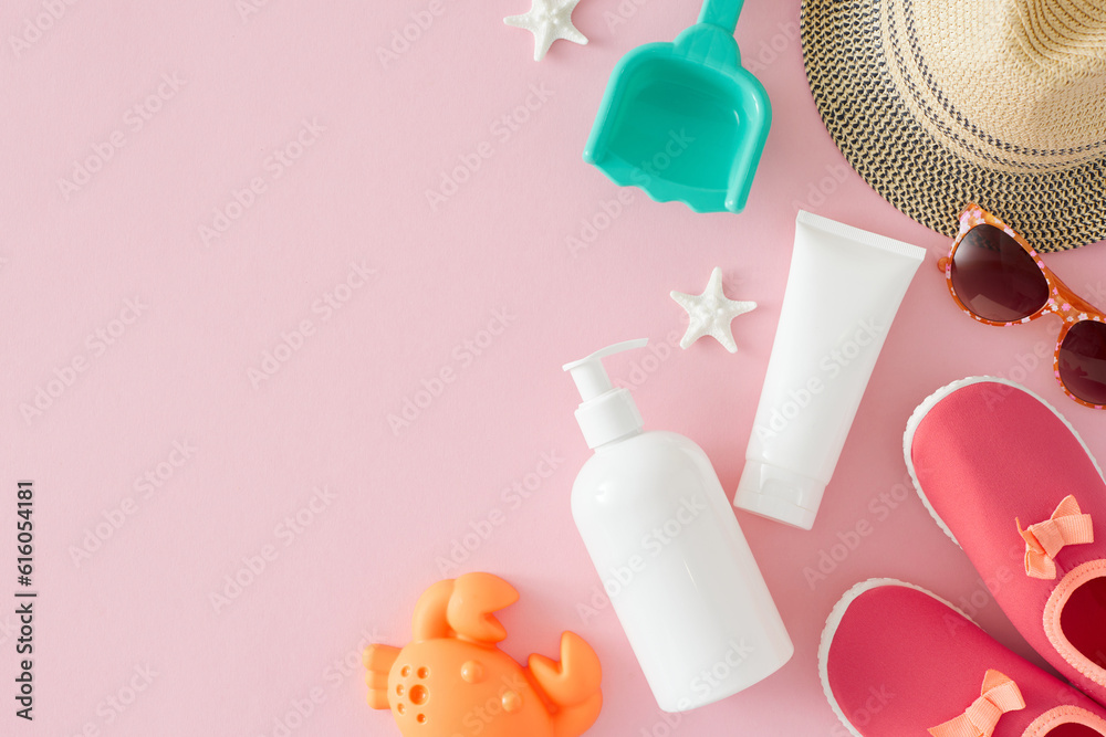 Sun protection cream concept for little ones. Top view photo of pump bottle, cream tube, beach toys, pink shoes, eyewear, panama hat, starfish on pastel pink background with space for promo or message