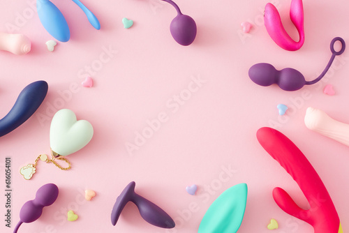 Adult erotic toys concept. Top view arrangement of vibrators, anal plugs, vaginal balls, colorful hearts on pastel pink background with empty space for text or advert