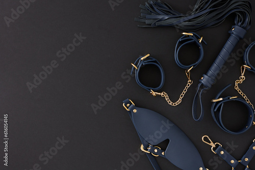 Concept of BDSM toys for sexual satisfaction. Top view composition of handcuffs, black mask, leather whip on black background with empty space for promo or text