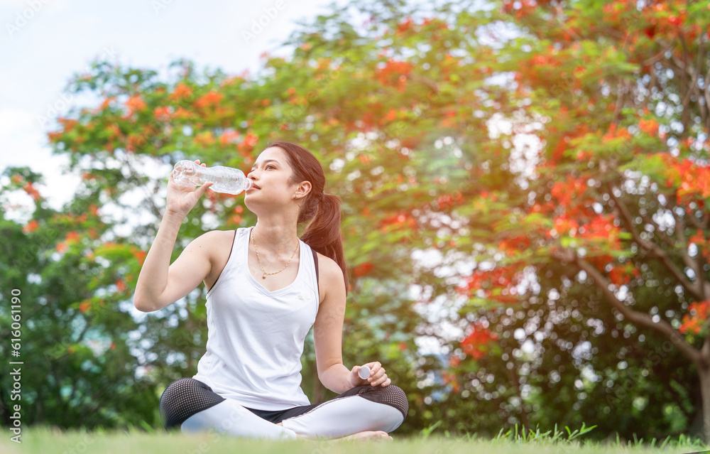 Young Indian woman sporting thirsty lifting water bottle after practicing yoga postures and stretching exercises to stay in shape in the park. Young Indian woman sporting thirsty lifting water bottle after practicing yoga postures and stretching exercises to stay in shape in the park.