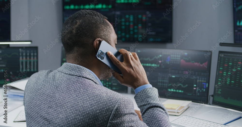 Φωτογραφία African American male stock trader talks by phone, works in broker office