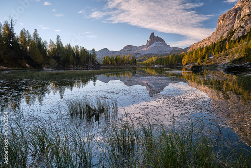 In an alpine setting, the majestic Dolomites are tinged with the warm autumn colors, while the imposing larches are colored with orange and gold, creating a reflections on the lake