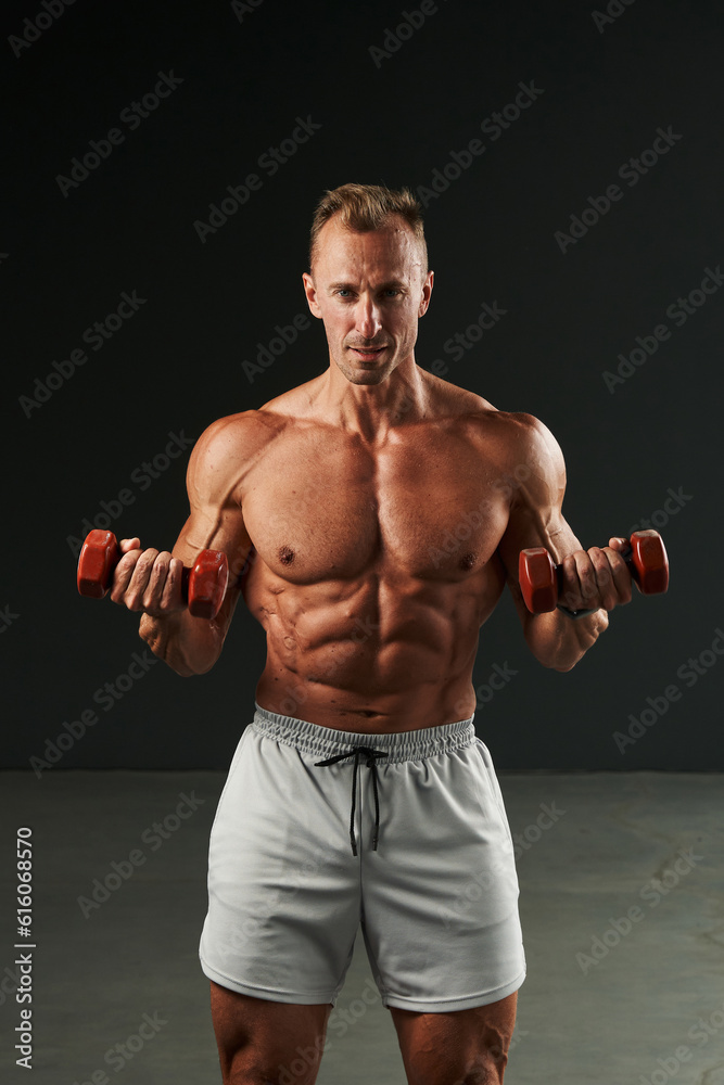caucasian man trains hard with dumbbells. beautiful body, perfectly pumped muscles, perfect abs, chest, shoulders, arms