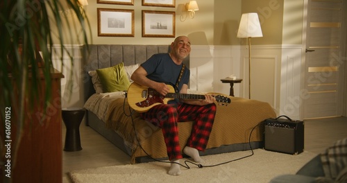 Elderly man sings and plays on electric guitar at home.