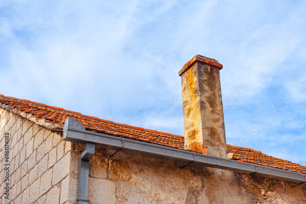 Old brick chimney on the roof of a house against the blue sky . Wall are made up of rectangular blocks