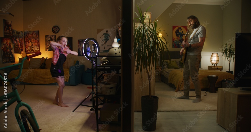 Man plays electric guitar in bedroom. Young girl records dance video for social networks on phone with ring lamp. View of two rooms or apartments separated by wall. Neighborhood and lifestyle concept.