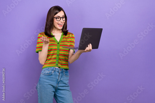 Photo of cheerful pleasant woman straight hairstyle wear colorful t-shirt look at laptop talk by video call isolated on purple background