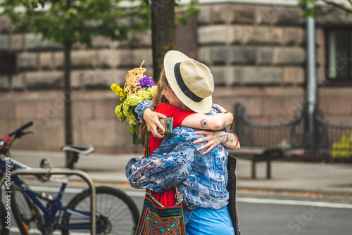 Young girls with tattoos and flowers meeting in the street and hugging for greetings, friendship and love concept