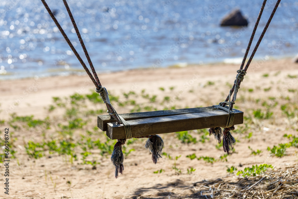 Old wooden swing on the ropes on the summer beach close-up. Swing in focus, background blurred. Old wooden swing on the ropes on the summer beach close-up. Swing in focus, background blurred.