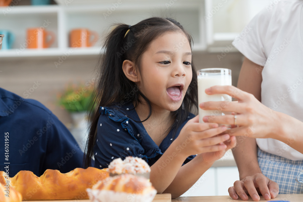 Asian little child girl receiving glass of milk from mother hand in kitchen at home. Happy smiling child girl learning and cooking in kitchen Asian little child girl receiving glass of milk from mother hand in kitchen at home. Happy smiling child girl learning and cooking in kitchen