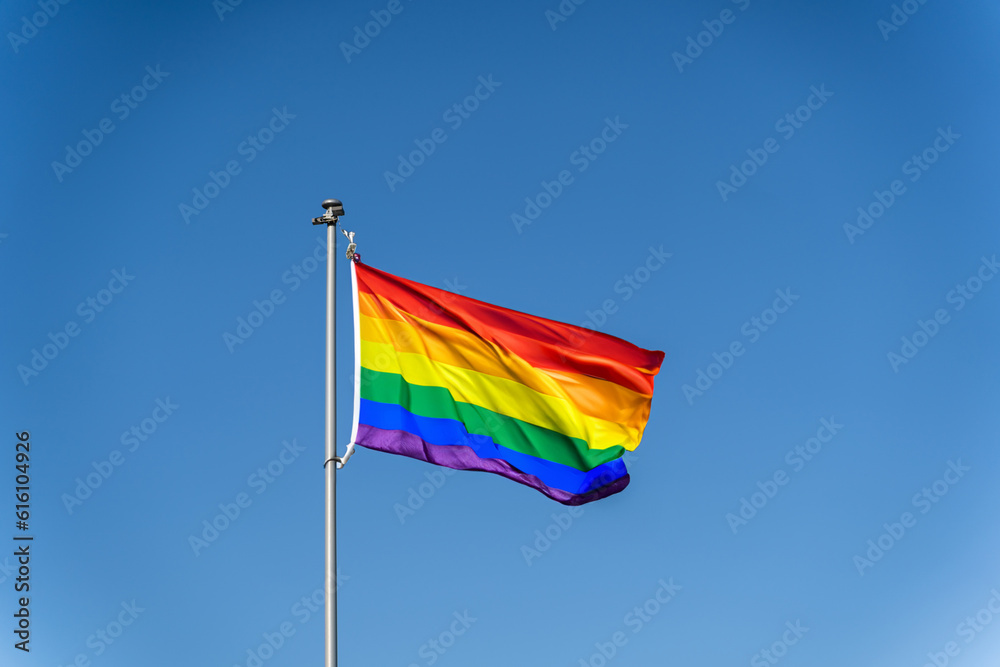 The rainbow flag of the LGBTQ community flies against blue clear sky The rainbow flag of the LGBTQ community flies against blue clear sky