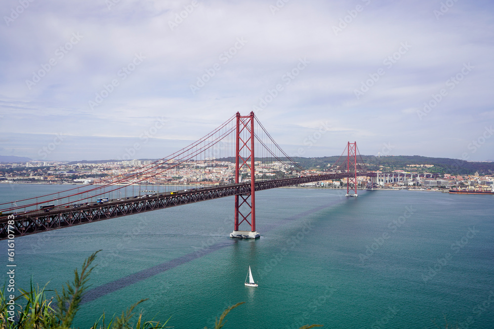 Fototapeta premium Lisbon, Portugal - March 2023: View of the April 25 Bridge and the city of Lisbon. 25 de Abril Bridge