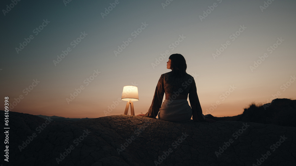 Silhouette of a thinking girl with a lamp on a mountain