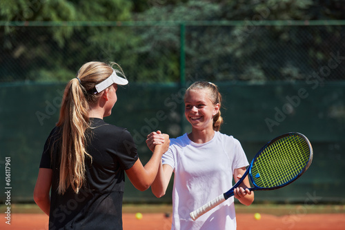 Two female tennis players shaking hands with smiles on a sunny day, exuding sportsmanship and friendship after a competitive match.