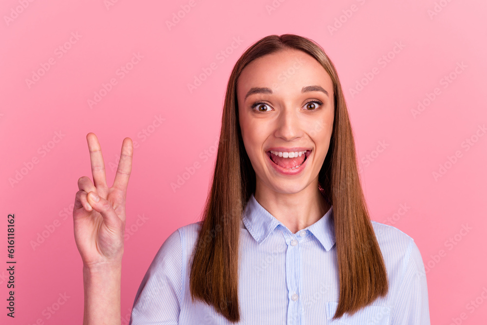 Young girl against pink wall makes peace gesture shows v sign body language concept Young girl against pink wall makes peace gesture shows v sign body language concept