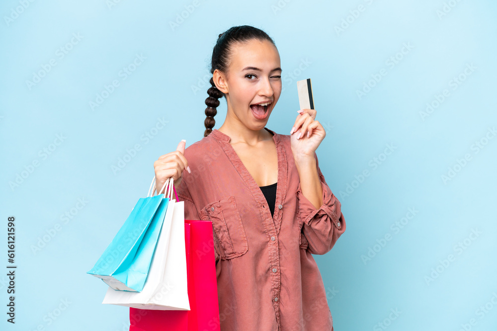 Obraz premium Young Arab woman isolated on blue background holding shopping bags and a credit card