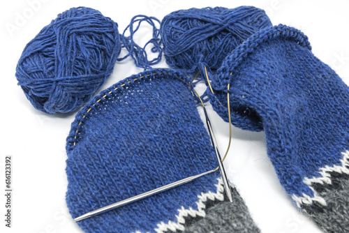 Blue wool yarn knitting on a metal needle with yarn balls on a white background, magic loop technique for knitted sleeves in progress