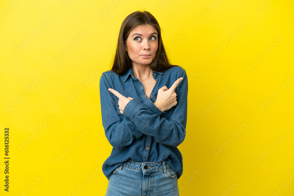 Young caucasian woman isolated on yellow background pointing to the laterals having doubts Young caucasian woman isolated on yellow background pointing to the laterals having doubts