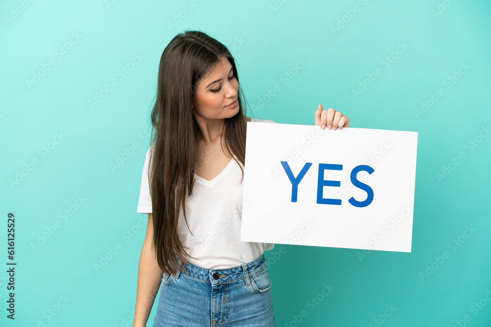Young caucasian woman isolated on blue background holding a placard with text YES Young caucasian woman isolated on blue background holding a placard with text YES